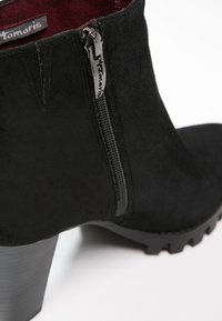 Bottines en daim noir avec une fermeture éclair sur le côté, finition mate, talon épais et semelle texturée pour une bonne adhérence. Doublées en tissu bordeaux.