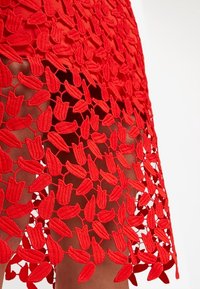 Jupe en dentelle rouge avec une broderie florale dense et des espaces ouverts laissant entrevoir la peau en dessous.