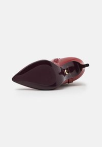 Scarpa alta con tacco in pelle rossa, con punta affusolata, caratterizzata da una finitura lucida sulla suola e una parte inferiore testurizzata per una migliore aderenza.