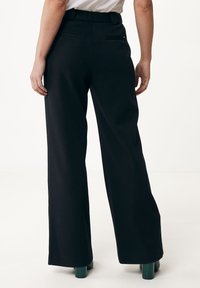 Pantalones anchos negros con una textura suave, con bolsillos traseros y una cinturilla alta, combinados con zapatos de tacón cuadrado verdes.