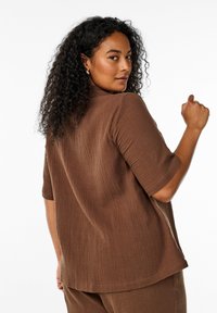 Brown, textured top with short sleeves, featuring a relaxed fit and a subtle, crinkled pattern. Back view showcases a stand collar.