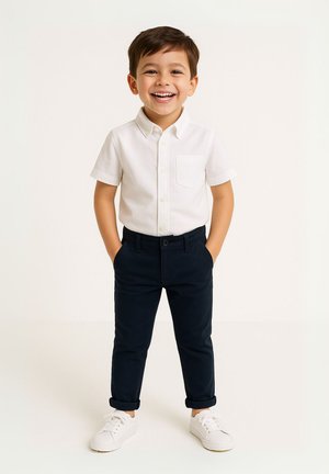 Chemise blanche à manches courtes avec une poche poitrine, associée à un pantalon bleu marine retroussé et des baskets blanches.