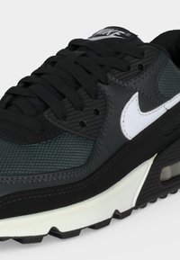 Sort og mørkegrøn Nike Air Max sneaker med hvid swoosh-logo, sorte snørebånd og synlig luftpolstring i sålen.