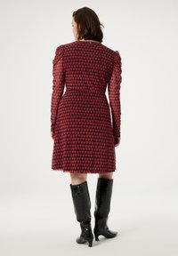 Rotes und schwarzes Kleid mit Herzmuster, durchsichtigen langen Ärmeln und einem Taillen-Detail. Kombiniert mit glänzenden schwarzen kniehohen Stiefeln.