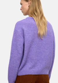 Fioletowy sweter dzianinowy z okrągłym dekoltem i ribbanym wykończeniem, o luźnym kroju i miękkiej teksturze. Prosty design, bez wzorów i ozdób.