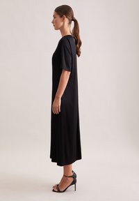 Czarna sukienka do kolan, z krótkimi rękawami i luźnym krojem. Gładka tkanina o prostym wzornictwie. Noszona z czarnymi sandałami na wysokim obcasie.