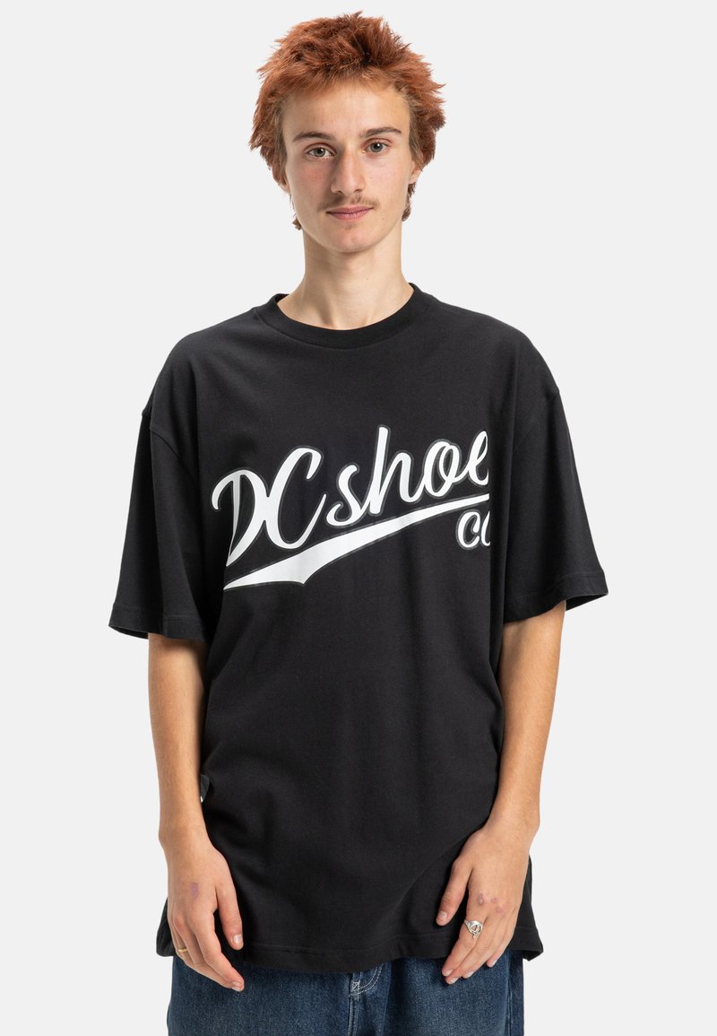 Černé oversized tričko vyrobené z bavlny, s velkým bílým potiskem loga vpředu. Hladký kulatý výstřih a krátké rukávy.