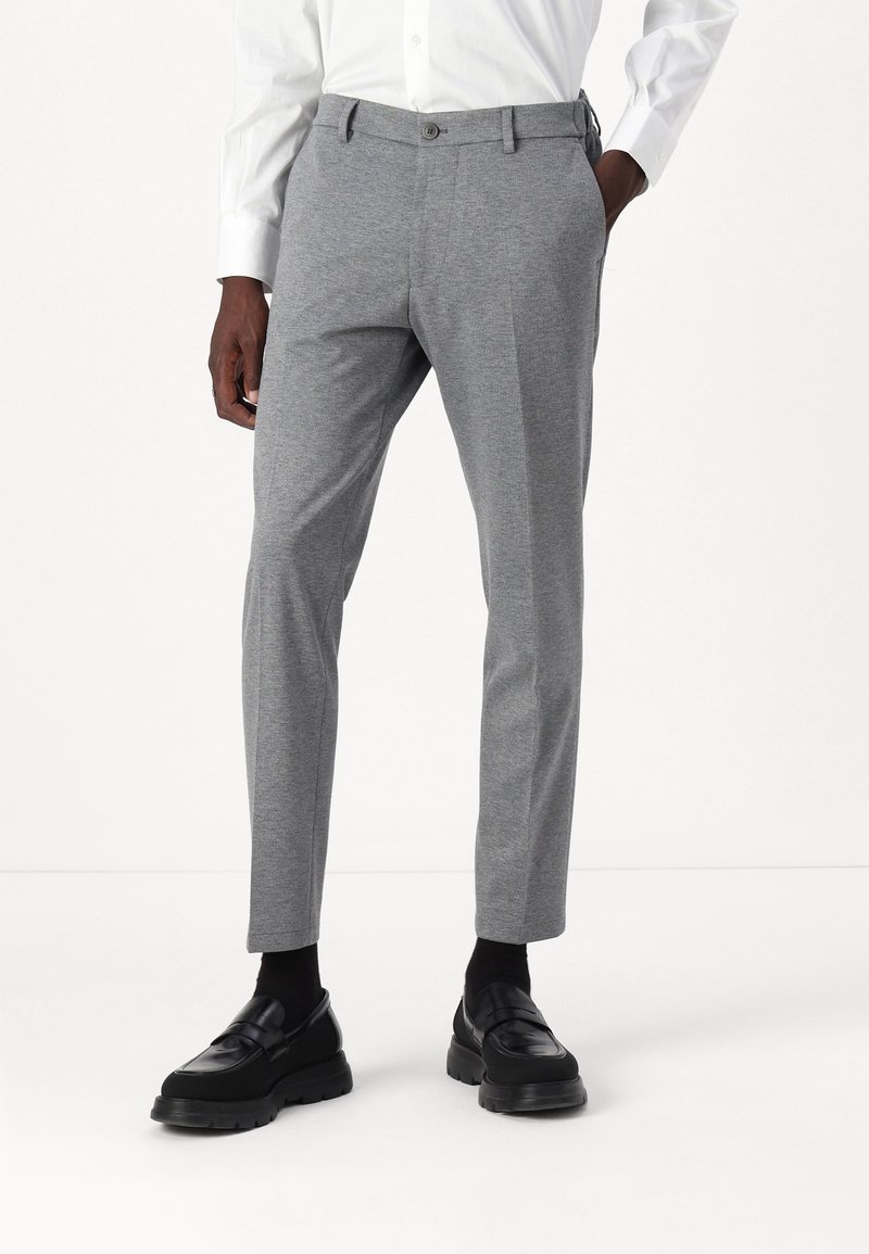 Szare spodnie w dopasowanym kroju, o gładkiej fakturze, z paskiem, guzikiem z przodu i bocznymi kieszeniami, w połączeniu z czarnymi mokasynami.