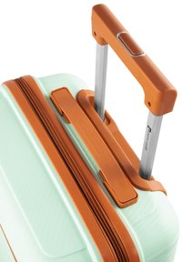 Harde koffer in lichtgroen met een gestructureerde afwerking; beschikt over een bruine handgreep en ritssluiting, en een zilverkleurig uitschuifbaar trolley systeem.