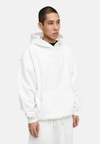 Weiße Kapuzen sweatshirt aus weichem Stoff. Mit einer Fronttasche, lockerer Passform und gerippten Bündchen. Kombiniert mit passenden Jogginghosen.