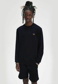 Felpa blu navy con logo ricamato dorato, colletto e polsini a costine, abbinata a pantaloni corti neri coordinati, dal taglio rilassato.