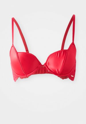 Czerwony satynowy biustonosz z wyściełanymi miseczkami, regulowanymi ramiączkami, koronkowym wykończeniem po bokach oraz zapięciem na haftkę z tyłu na białym tle.