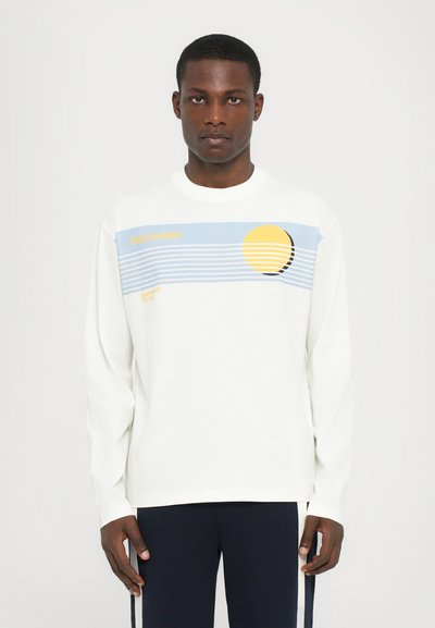 Chemise à manches longues blanche avec un graphisme bleu et jaune, des rayures horizontales, le texte "Holzweiler" et un motif de soleil jaune rond.