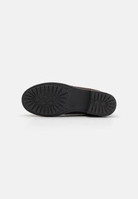 Suela de goma negra con un patrón de tread que presenta formas circulares y cruzadas; acabado texturizado con un talón plano y lados reforzados.