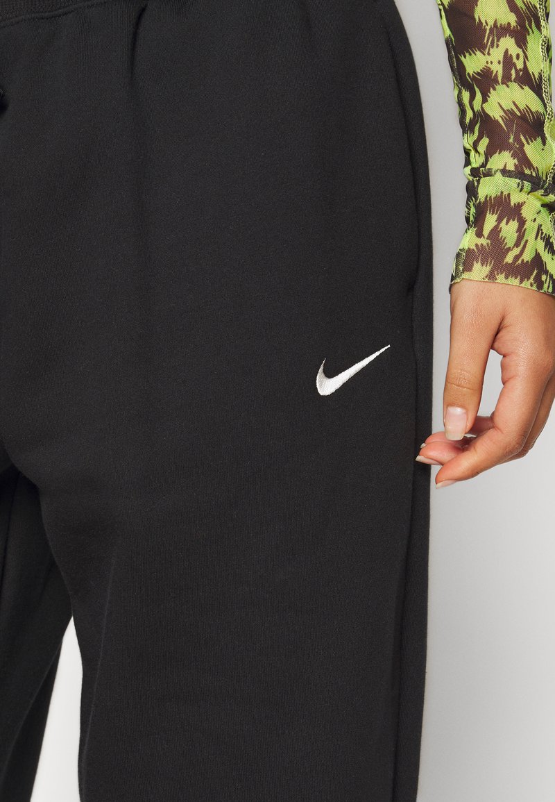 Schwarze Jogginghosen aus weichem Stoff mit elastischem Bund. Mit kleinem weißen Nike-Logo auf der linken Seite. Nahaufnahme der Textur.
