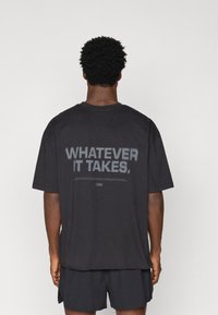 Čierne bavlnené tričko s krátkymi rukávmi a okrúhlym výstrihom. Text na chrbte znie "ČO TREBA", v tučných sivých písmenách.