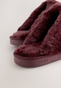 Paire de chaussons bordeaux duveteux avec semelles épaisses, design à bout ouvert et matière douce en peluche pour usage intérieur.