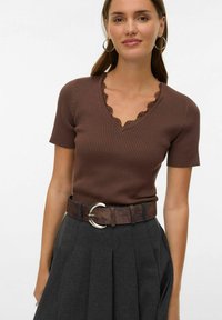 Pruun soonikuga lühikeste varrukatega top kaarelise V-kaelusega, mida on kombineeritud halli voltidega seelikuga ja pruuni vöökohaga, millel on hõbedane ümmargune pandl.