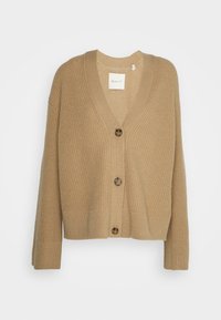 Beżowy dziergany kardigan z dekoltem w serek, pięcioma brązowymi guzikami oraz prążkowaną fakturą na rękawach i na dole. Wewnątrz widoczna metka z nazwą marki.