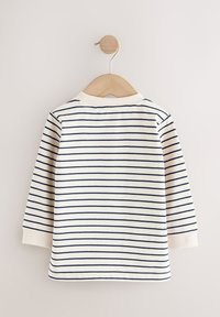 Maglietta bianca a maniche lunghe per bambino con sottili righe orizzontali blu navy, polsini e colletto a coste, appesa a una gruccia di legno su uno sfondo chiaro.