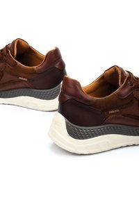 Zapatillas de cuero marrón con detalles de malla, que presentan una suela texturizada gris oscuro y una base acolchada blanca. Sin logotipos visibles.