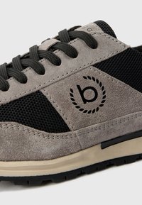 Adidași din suede gri cu panouri din plasă neagră, logo rotund negru și șireturi gri. Prezintă o talpă din cauciuc cu accente de culoare deschisă.