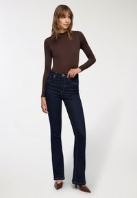 Body a maniche lunghe marrone, abbinato a jeans flare blu scuro con cuciture e tasche in vista, completato da tacchi a punta marroni.