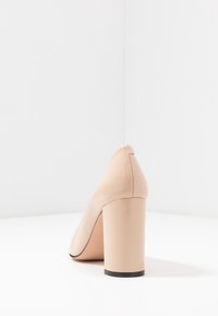 Escarpin en cuir verni nude à talon haut, avec un bout arrondi et un talon épais, texture lisse avec un léger éclat, sans ornementation visible.