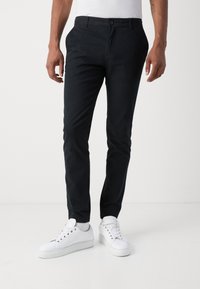 Heren zwarte chinos van een katoenmix, tapered fit, met zijzakken en een frontale knoopsluiting, gecombineerd met witte sneakers.