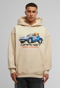 Beige hettegenser med en blå bilgrafikk og en bjørn, trykket tekst "MARKET Ultimate Performance" i rødt. Kengurulomme.