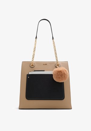 Beżowa torebka tote z ekologicznej skóry z czarną kieszenią z przodu, złotymi łańcuszkami do noszenia oraz brązowym futrzanym pomponem. Minimalistyczny design z kontrastującymi kolorami.