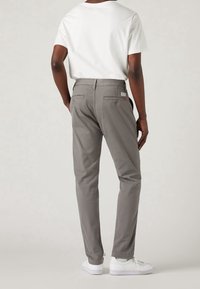 Pantaloni di cotone grigi con taglio slim, dotati di due tasche posteriori e un'etichetta con il marchio. Abbinati a sneakers bianche e a una t-shirt bianca semplice.