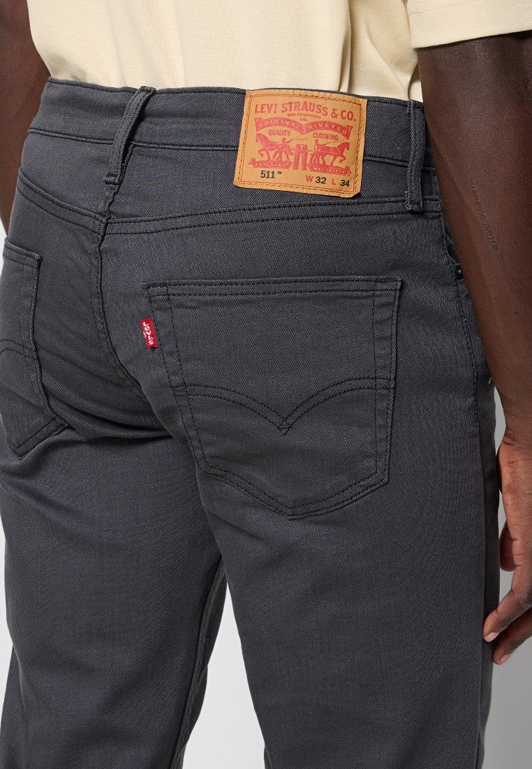 Donkergrijze Levi's 511 jeans gedragen door een persoon, zichtbare stiksels van de achterzak, rode Levi's-label en leren merkpatch met maatdetails.