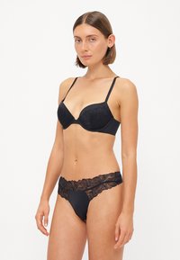 Schwarzer Spitzen-BH mit Bügel und verstellbaren Trägern, kombiniert mit passenden, mit Spitze verzierten schwarzen Panties. Glatte Textur und florale Details.