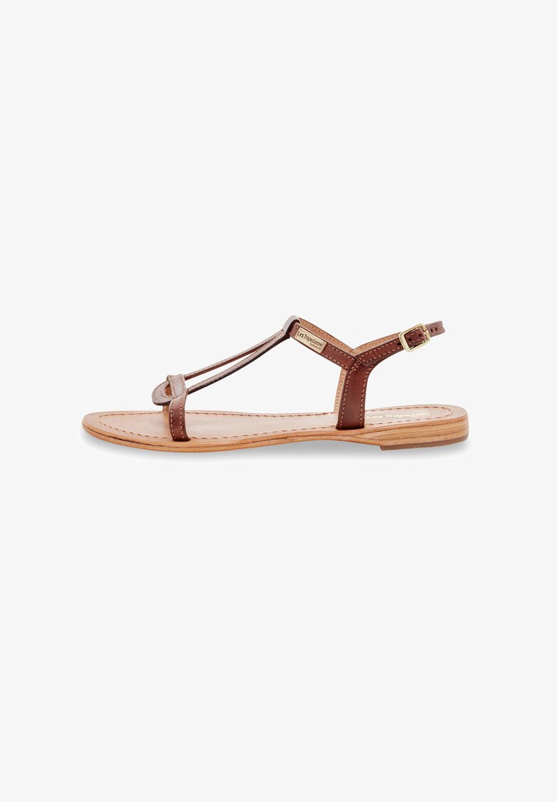 Sandale plate en cuir marron avec un design à T, un bout rond, une boucle à la cheville et une semelle de couleur naturelle cousue. Style minimaliste et ouvert.