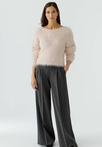 Un pull moelleux rose pâle avec un décolleté large, assorti à un pantalon large à rayures grises. La texture douce et la coupe décontractée définissent l'ensemble.