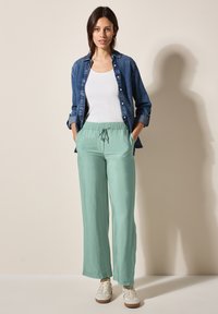 Pantalons larges vert clair avec une taille élastique, associés à un haut en tank top blanc et une chemise en denim bleu à boutons. Baskets blanches casual.