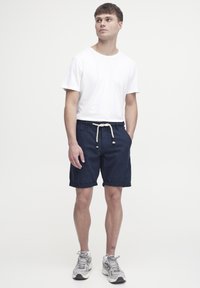 Pantalones cortos azul marino con dobladillos enrollados y cintura con cordón, combinados con una camiseta blanca sencilla y zapatillas deportivas gris claro.