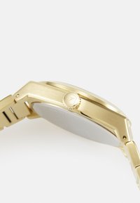 Reloj de metal dorado con una elegante caja rectangular, corona de pulsador texturizada y un acabado pulido, que complementa un diseño de correa con eslabones.