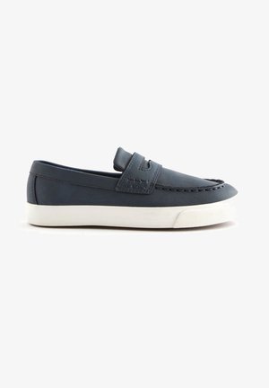 Mocassin slip-on bleu marine avec semelle en caoutchouc blanc et couture décorative, vue de côté sur fond blanc.