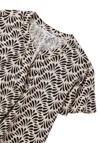Blusa a maniche corte color crema con un motivo a foglia nera, dotata di scollatura rotonda e una fila di bottoni sul davanti. Tessuto morbido e leggero.