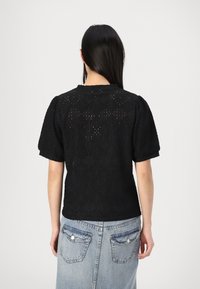 Camicia nera con texture, maniche a puff corte, caratterizzata da un motivo decorativo e un collo rotondo, abbinata a una gonna di jeans blu chiaro.