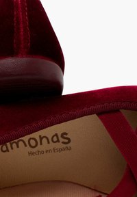 Zapatilla plana de terciopelo burdeos con punta redonda, correa elástica y plantilla texturizada marcada "Hecho en España." Suela de goma suave.