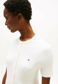 Biały sweter z dzianiny z wyraźnym wzorem w diamenty, ribbowanym kołnierzykiem, krótkimi rękawami i małym logo na piersi.