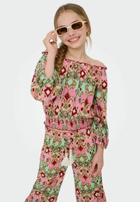 Completo a due pezzi con un motivo floreale in verde, rosa e rosso. Top a spalle scoperte con maniche a campana e vita arricciata; pantaloni con nappine.