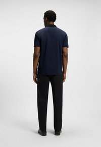 Granatowa koszulka polo z teksturowanym wzorem, krótki rękaw i czarny kołnierzyk, zestawiona z czarnymi spodniami prostymi i czarnymi butami.