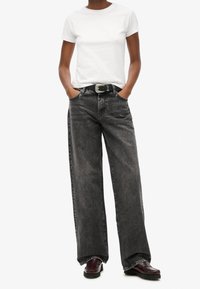 Camiseta blanca de algodón combinada con vaqueros negros de tiro alto y corte holgado. Cinturón negro con hebilla plateada. Se observan zapatos burdeos.