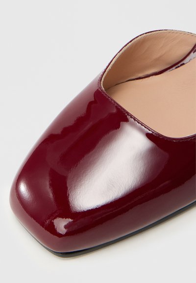 Chaussure en cuir verni bordeaux avec un bout carré et un design à découpe basse ; texture lisse avec une finition brillante et un intérieur beige.