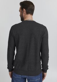 Mørkegrå strikkegenser med et teksturert mønster øverst, ribbestrikkede mansjetter og hem, sett bakfra. Båret med blå jeans.