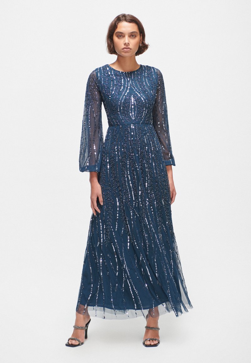 Robe bleu marine avec de longues manches transparentes, embellie de sequins dans des motifs en spirale. Design à longueur de sol avec une taille ajustée.